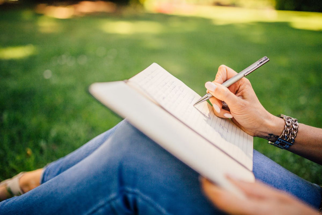 a notebook propped up on a white woman's bent knees as she writes in it with a pen